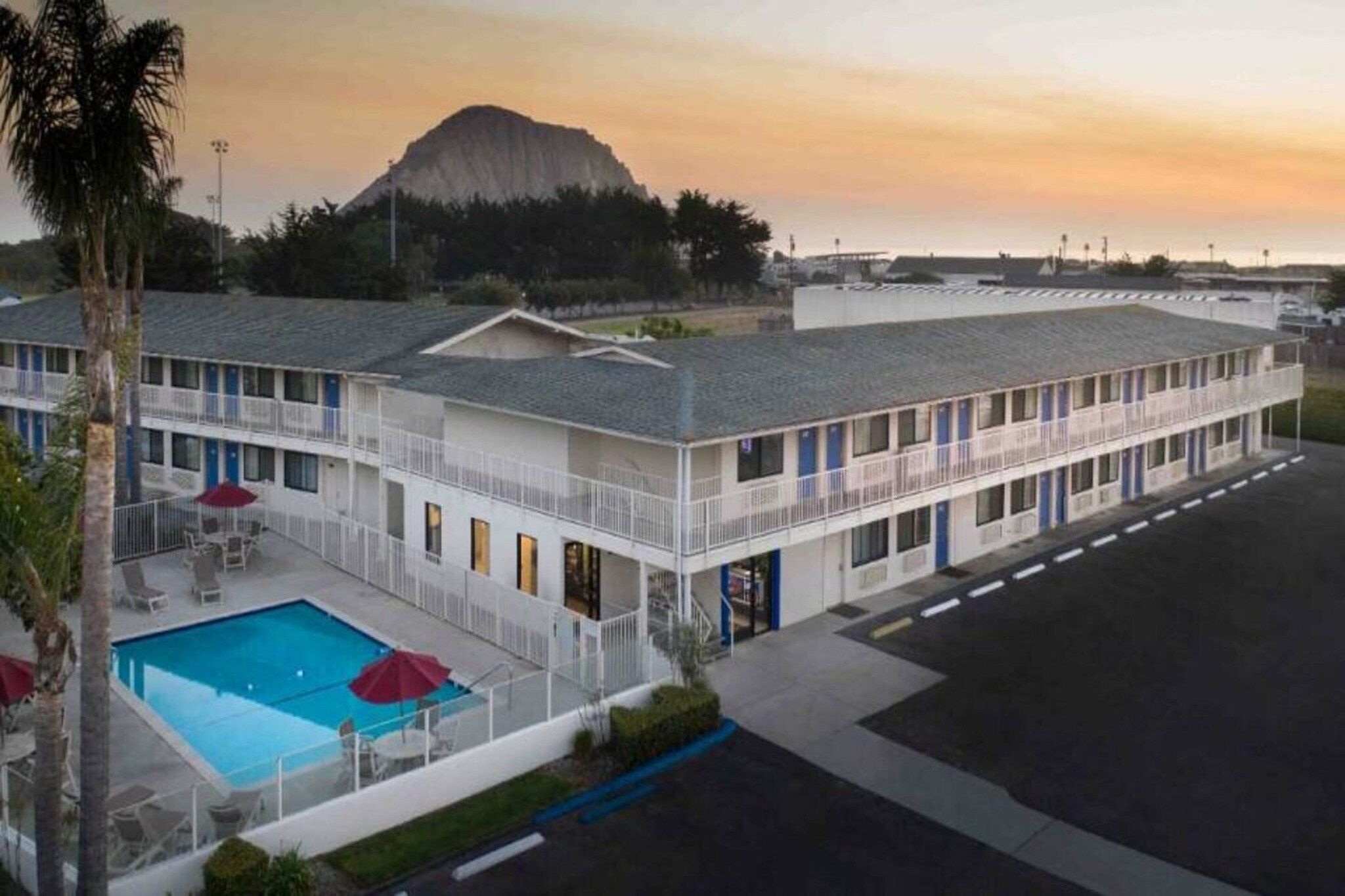 Um motel com piscina, uma montanha ao fundo e estacionamento.