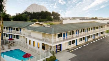 Een motel met een zwembad, meerdere balkons en een berg op de achtergrond.