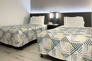 A hotel room with two beds, each with a patterned bedspread, a bedside table with a lamp, and a wall-mounted TV. - Spacious 2 Full Beds ||Pool|Free Wifi (Morro Bay)