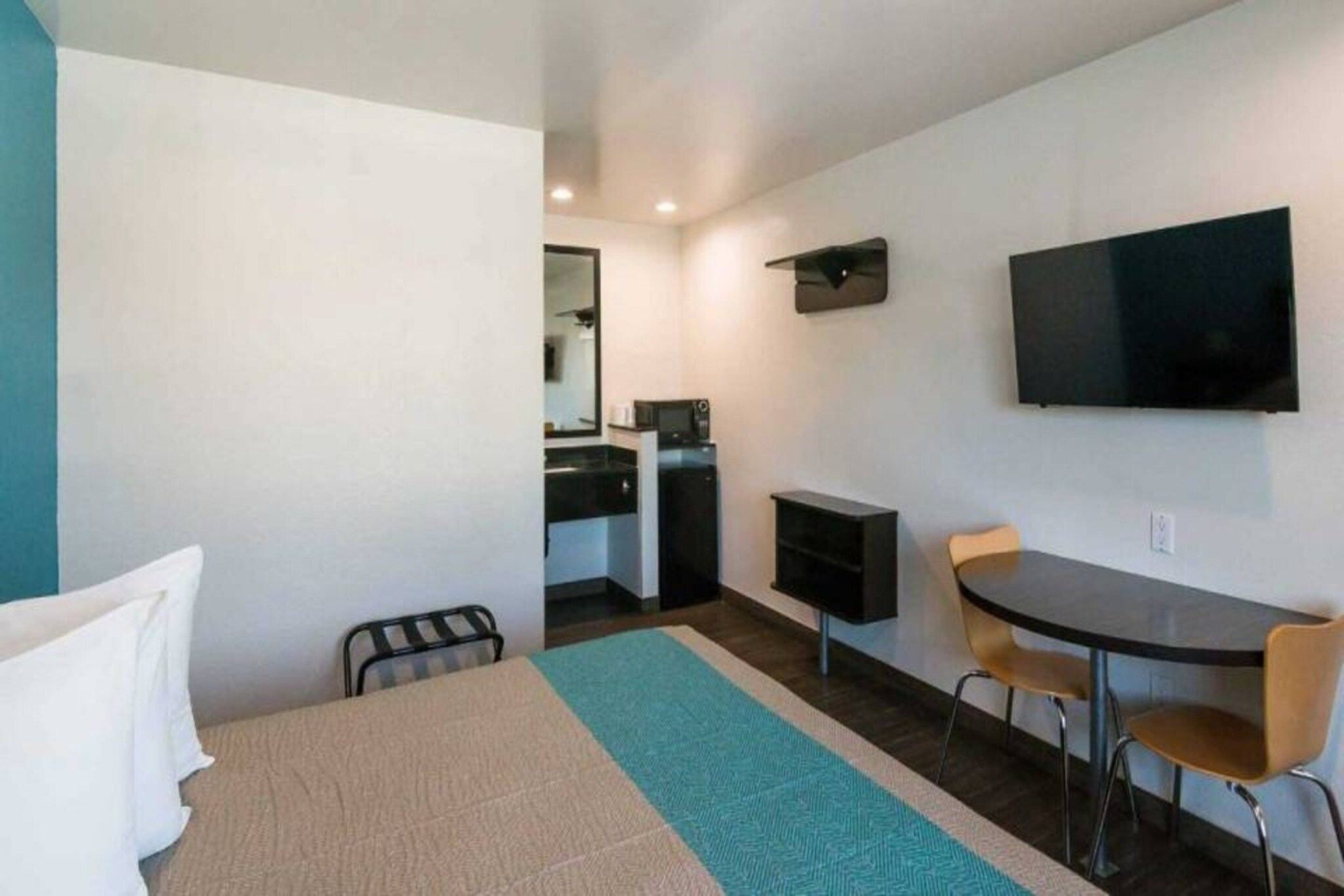 A hotel room with a bed, a desk, a chair, a television, and a kitchenette.