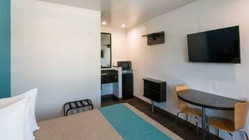 A hotel room with a bed, a desk, a chair, a television, and a kitchenette.