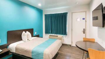 Quarto de hotel com cama, escrivaninha, cadeira, televisão e janela com cortinas.