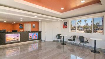 A hotel lobby with a reception desk, a large window with a view, and a seating area with tables and chairs.