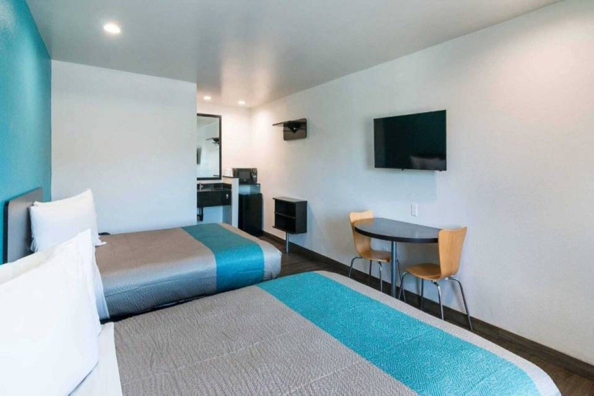 A hotel room with a bed, a desk, a chair, a television, and a small kitchenette.