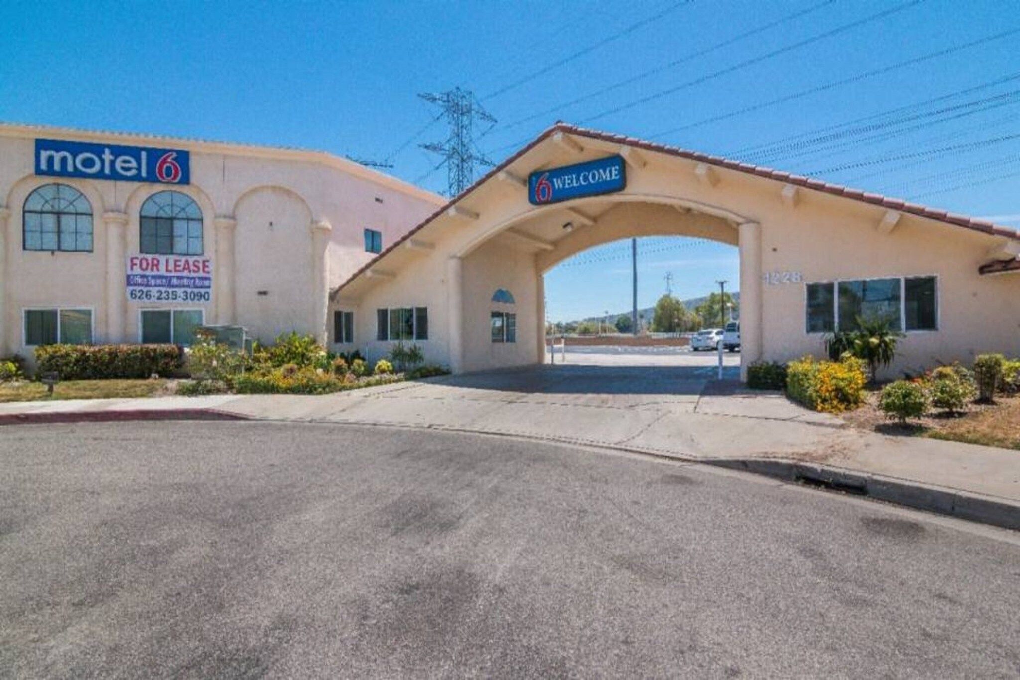 A motel with a 'Welcome' archway, a 'For Lease' sign, and a clear sky.