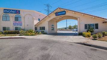 A motel with a 'Welcome' archway, a 'For Lease' sign, and a clear sky.