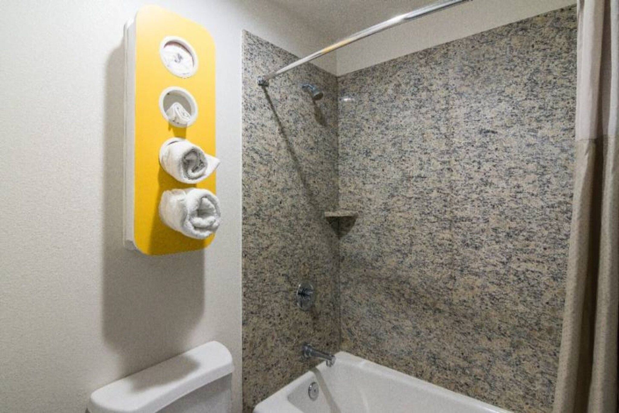 A bathroom with a shower, a toilet, and a towel rack with towels.