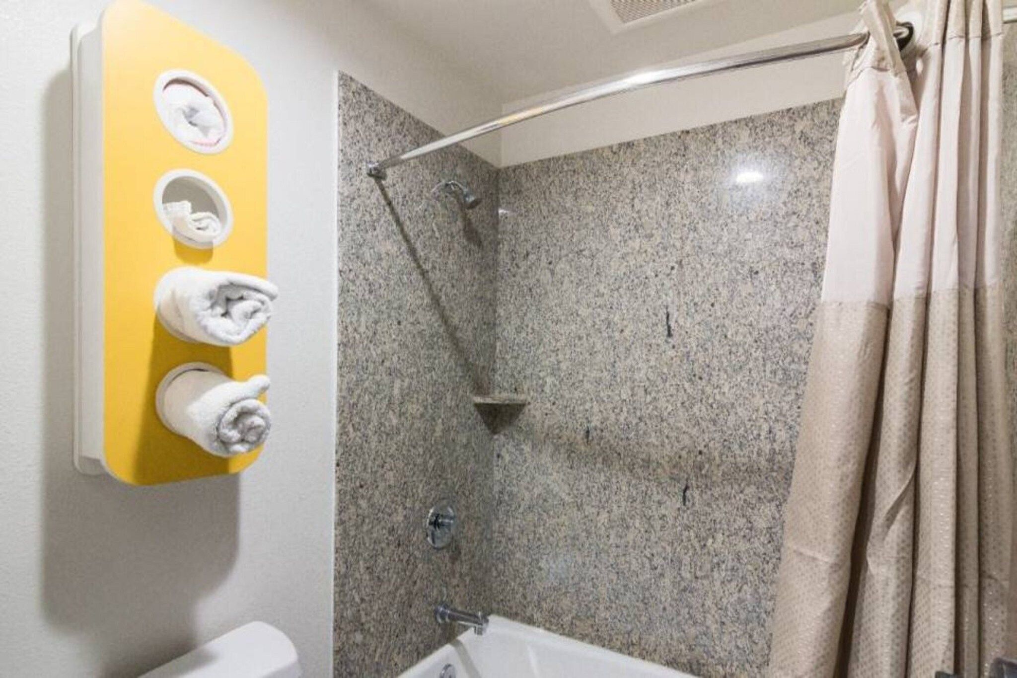 Un baño con ducha, inodoro y un perchero con tres toallas.