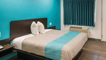 A hotel room with a bed, a nightstand, a window with curtains, and a wall heater.