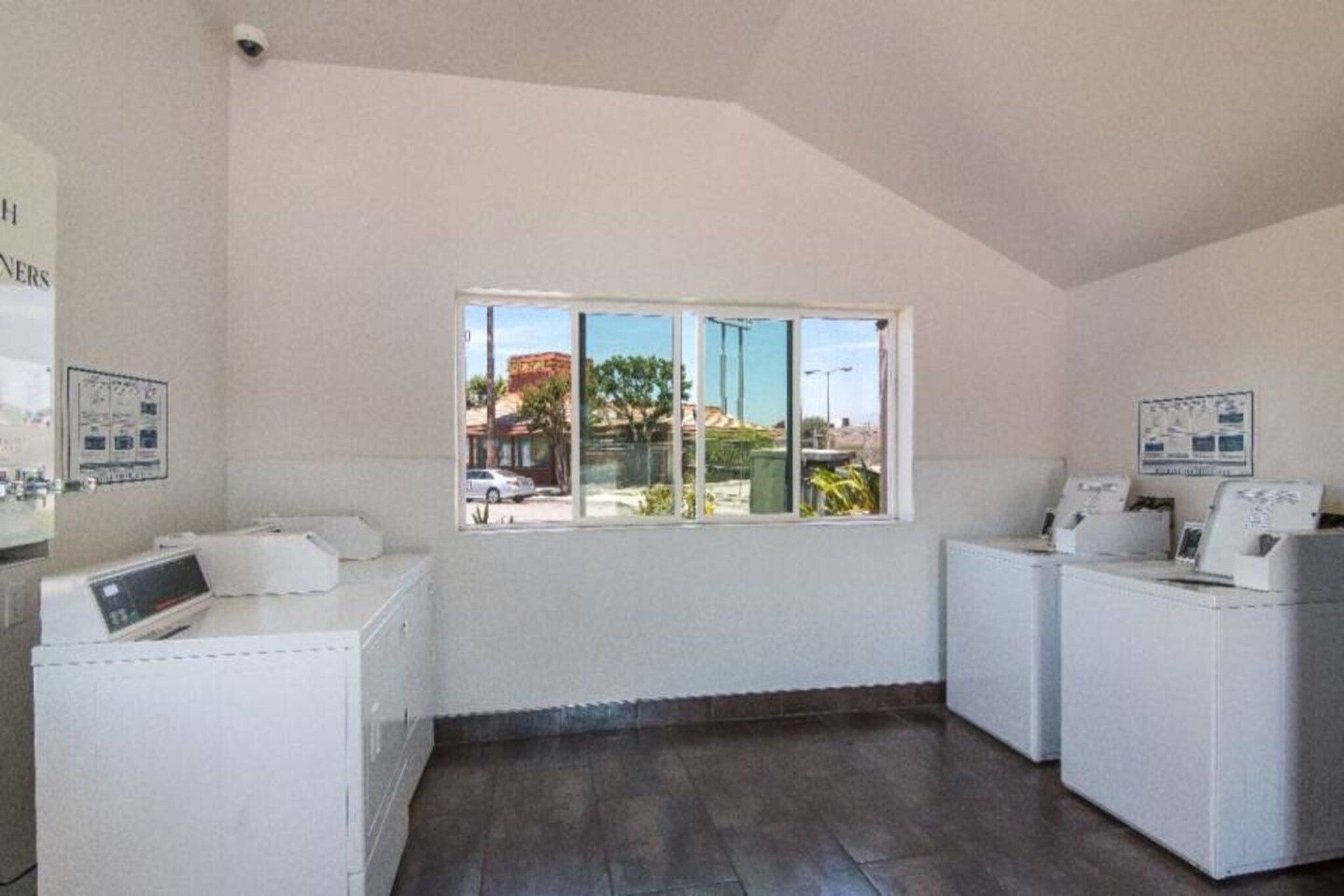 A laundry room with two washing machines, a dryer, and a window with a view of the outside.
