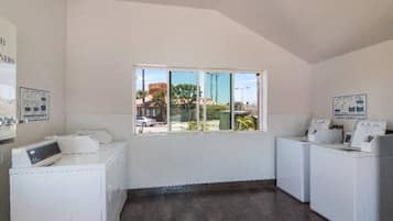 A laundry room with two washing machines, a dryer, and a window with a view of the outside.