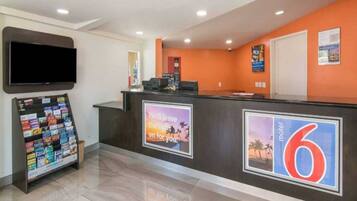 A hotel reception area with a digital display, a magazine rack, and a wall-mounted sign.