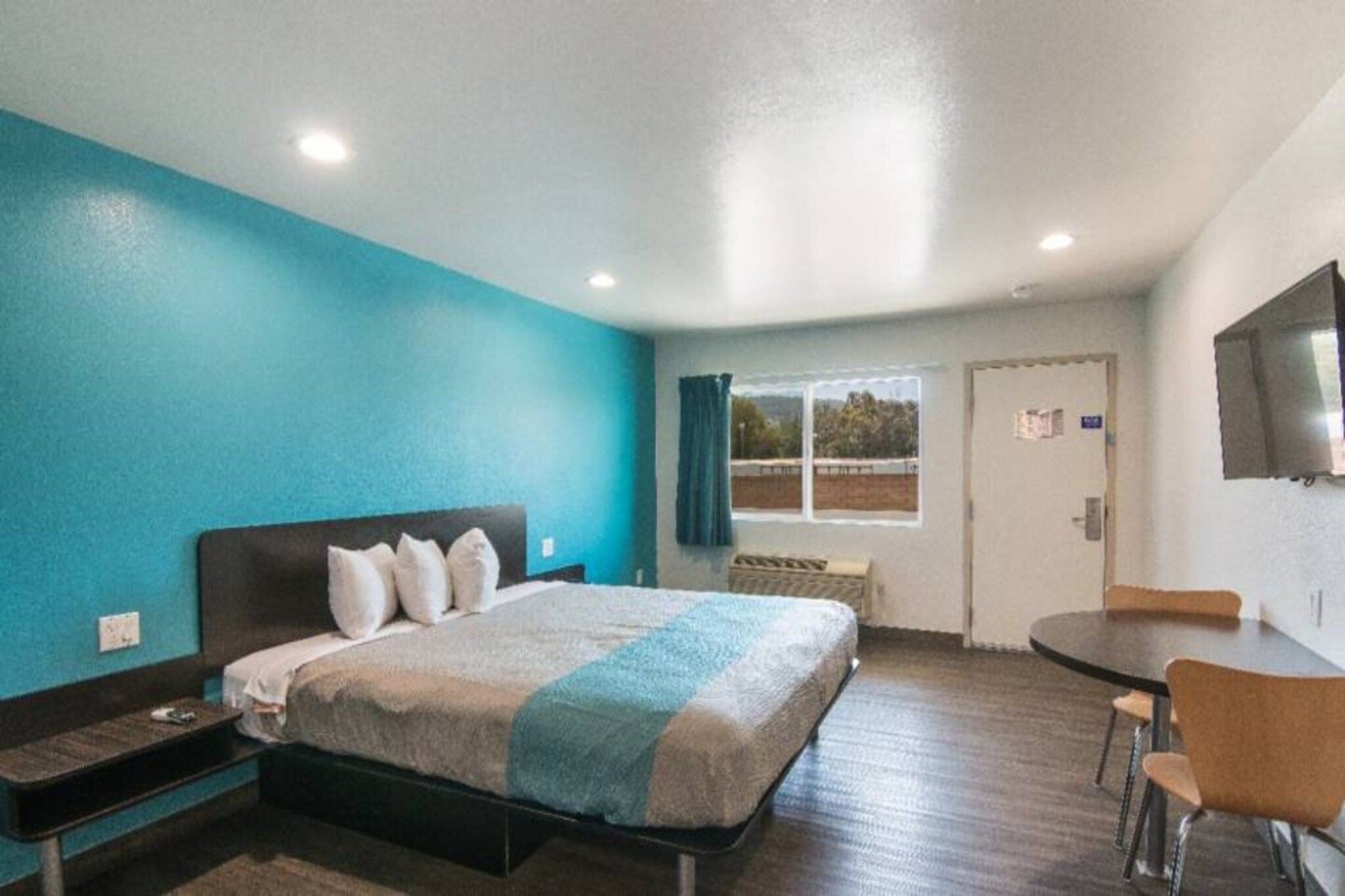 A hotel room with a bed, a desk, a chair, a TV, and a window with curtains.