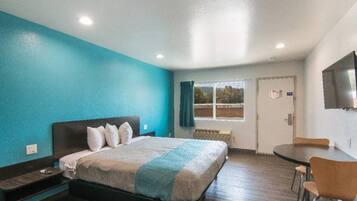 A hotel room with a bed, a desk, a chair, a TV, and a window with curtains.