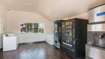 A room with a vending machine, a white refrigerator, and a window with a view of buildings.