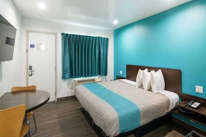 Een hotelkamer met een bed, een bureau, een stoel, een raam met gordijnen en een wand met een lichtschakelaar.