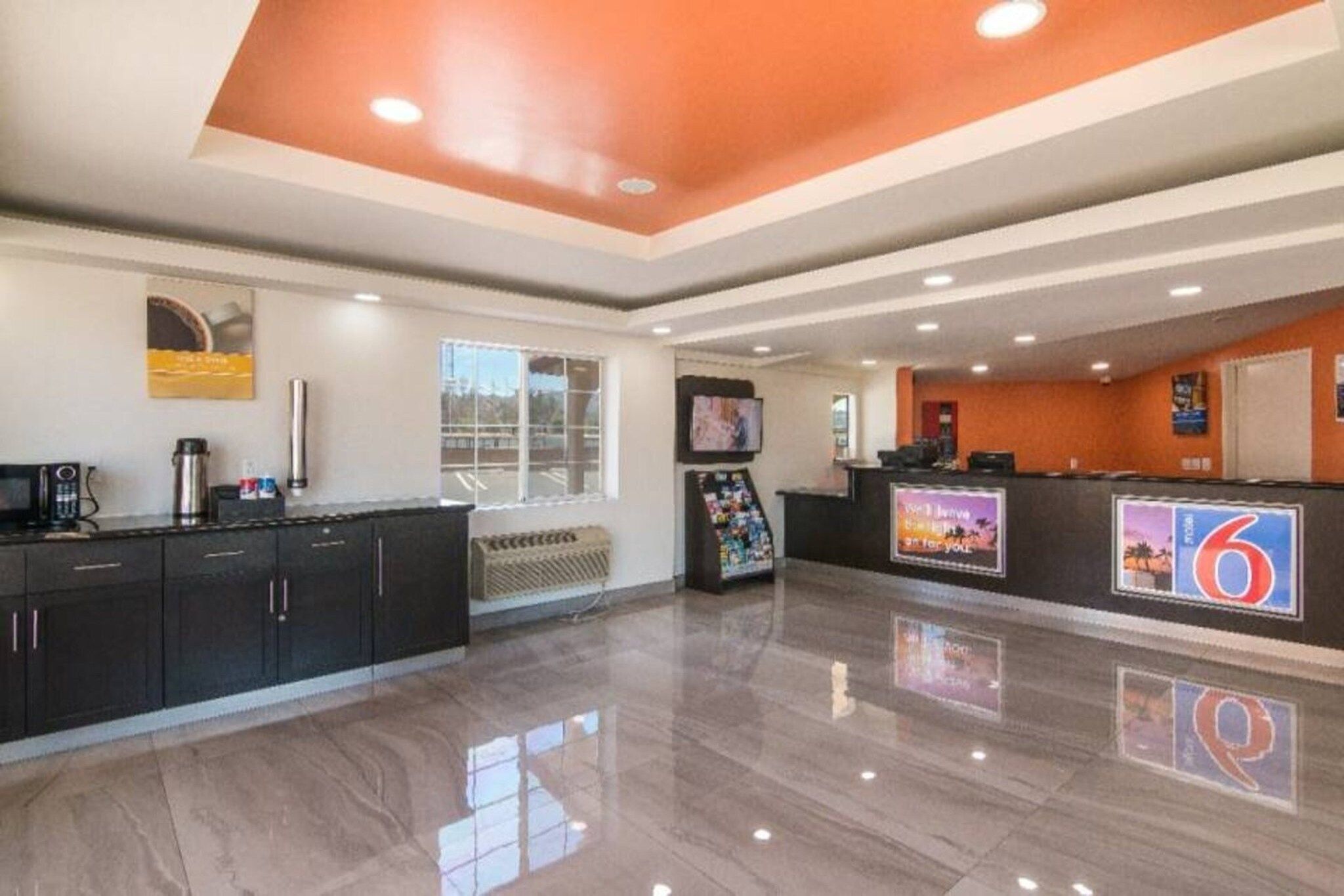 A hotel lobby with a reception desk, a coffee machine, a TV, and a seating area with a sofa.