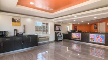 A hotel lobby with a reception desk, a coffee machine, a TV, and a seating area with a sofa.