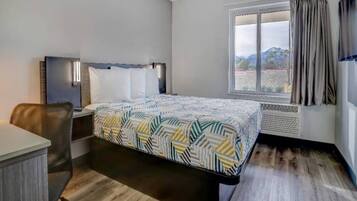 Ein Hotelzimmer mit einem Bett, einem Schreibtisch, einem Stuhl, einem Fenster mit Vorhängen und Blick ins Freie.