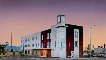 A multi-story hotel with a prominent '6' sign, a parking lot, and a mountain backdrop.