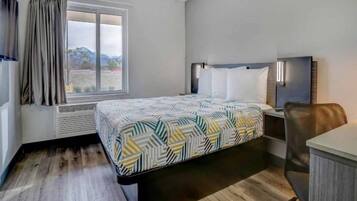 A hotel room with a bed, a desk, a chair, a TV, and a window with curtains.