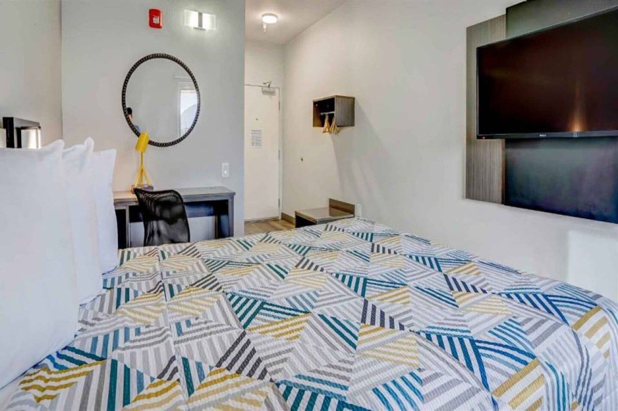 A hotel room with a bed, a desk, a chair, a mirror, a television, and a small closet.