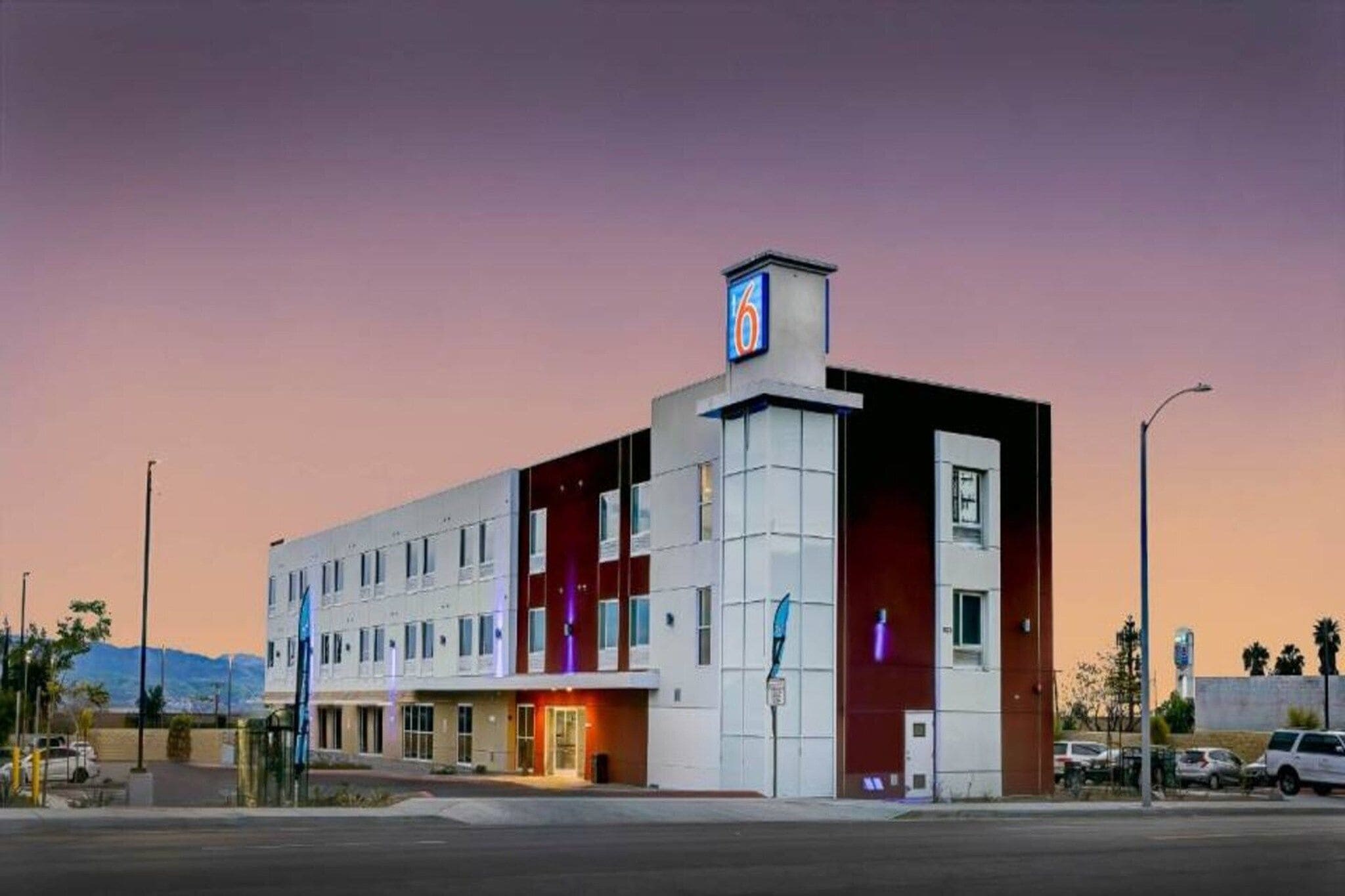 Ein mehrstöckiges Hotel mit einem auffälligen '6' Schild, einem Parkplatz und einem Berg im Hintergrund.