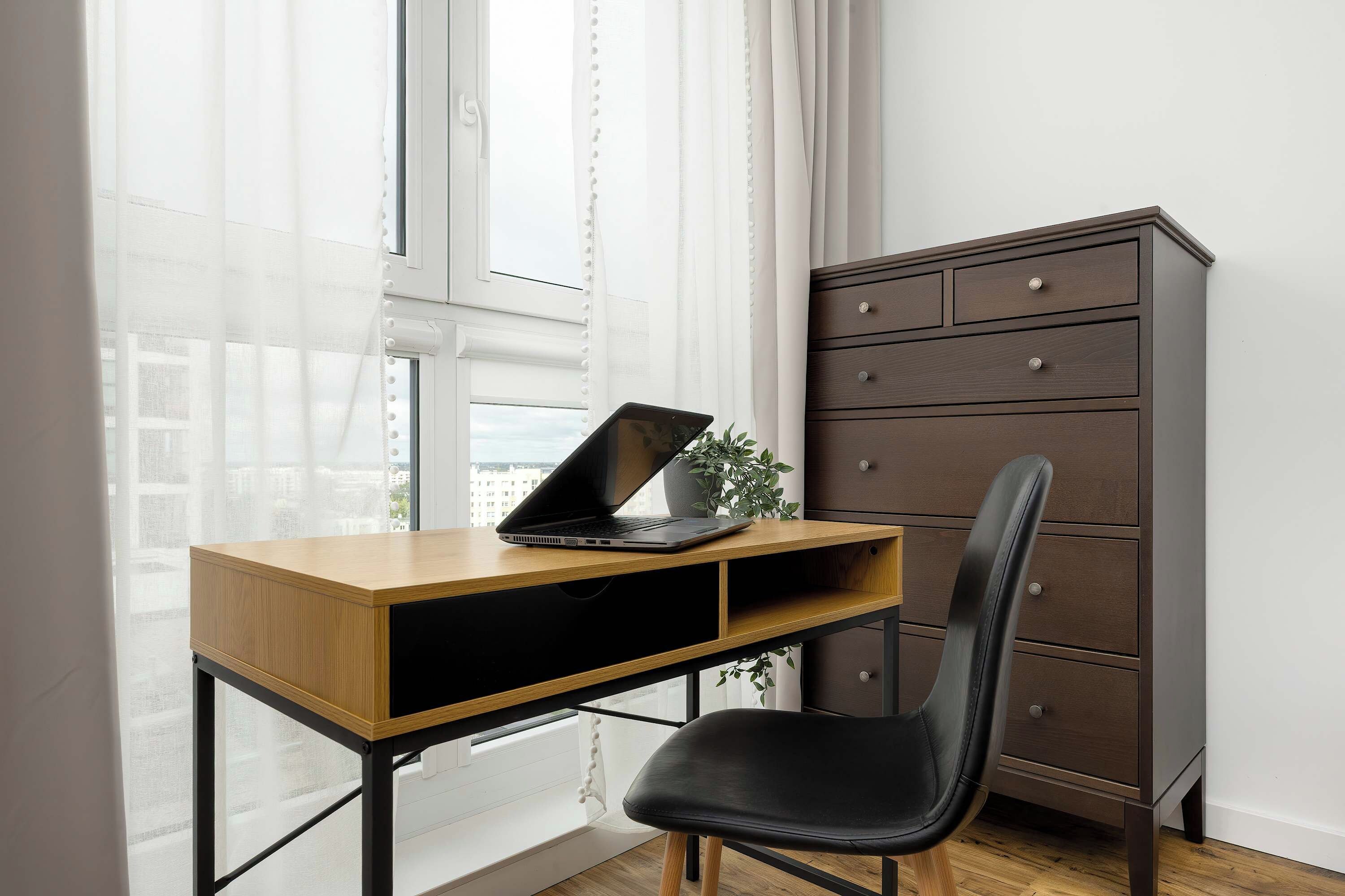 A room with a wooden desk, a laptop, a black chair, and a dark brown filing cabinet.