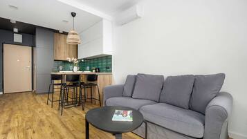 Ein modernes Wohnzimmer mit einem grauen Sofa, einem kleinen runden Tisch und einer Küchenzeile mit Esstisch und Stühlen.