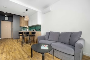 Ein modernes Wohnzimmer mit einem grauen Sofa, einem kleinen runden Tisch und einer Küchenzeile mit Esstisch und Stühlen.