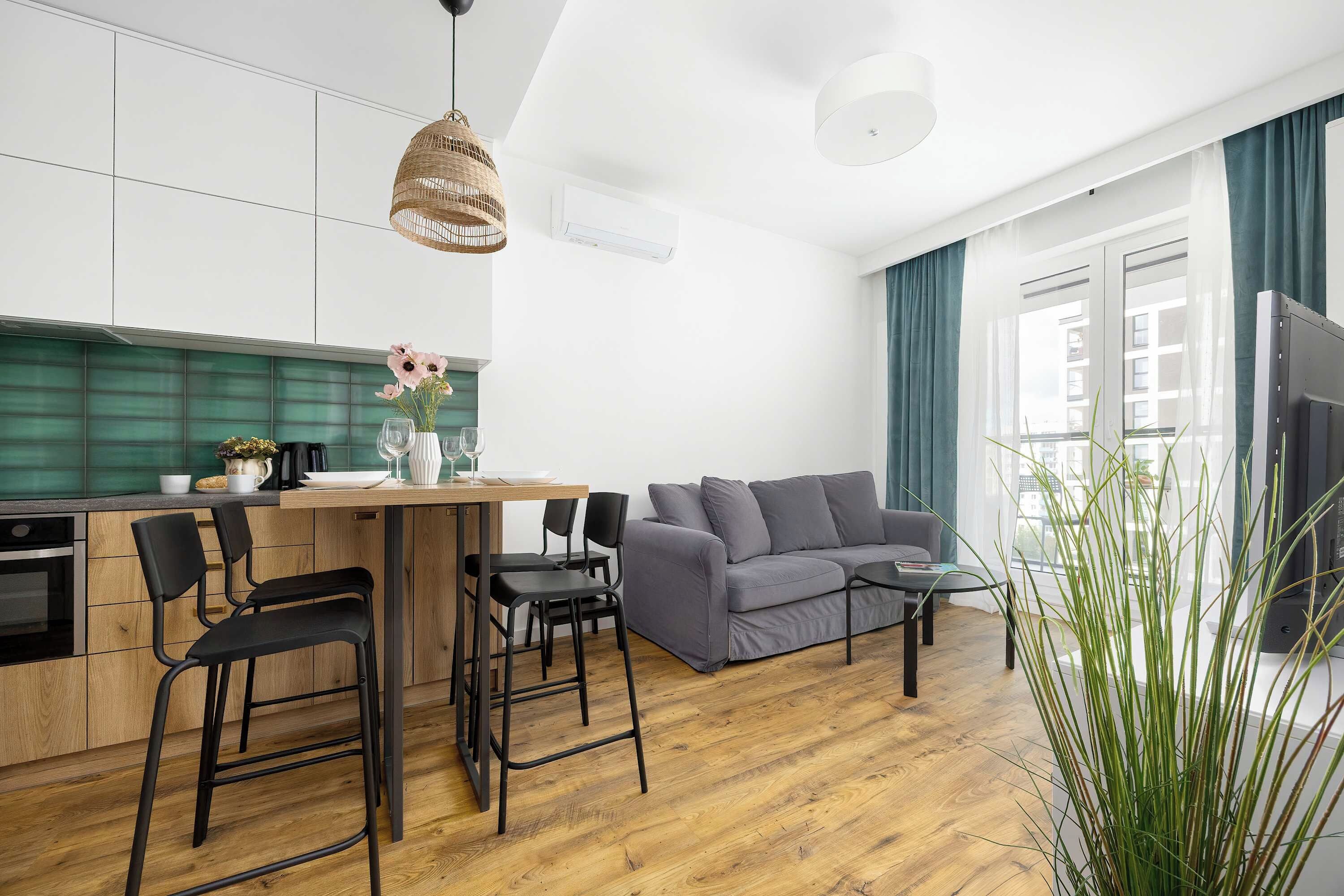 A modern kitchen with a dining area, a grey sofa, and a large window with curtains.