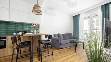 A modern kitchen with a dining area, a grey sofa, and a large window with curtains.