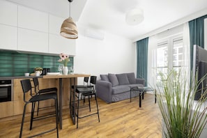 Eine moderne Küche mit Essbereich, einem grauen Sofa und einem großen Fenster mit Vorhängen.