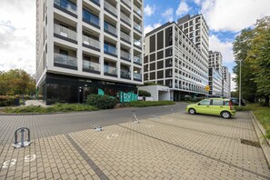 Ein modernes Gebäude mit Glasfassade, davor ein grünes Auto und ein klarer Himmel.