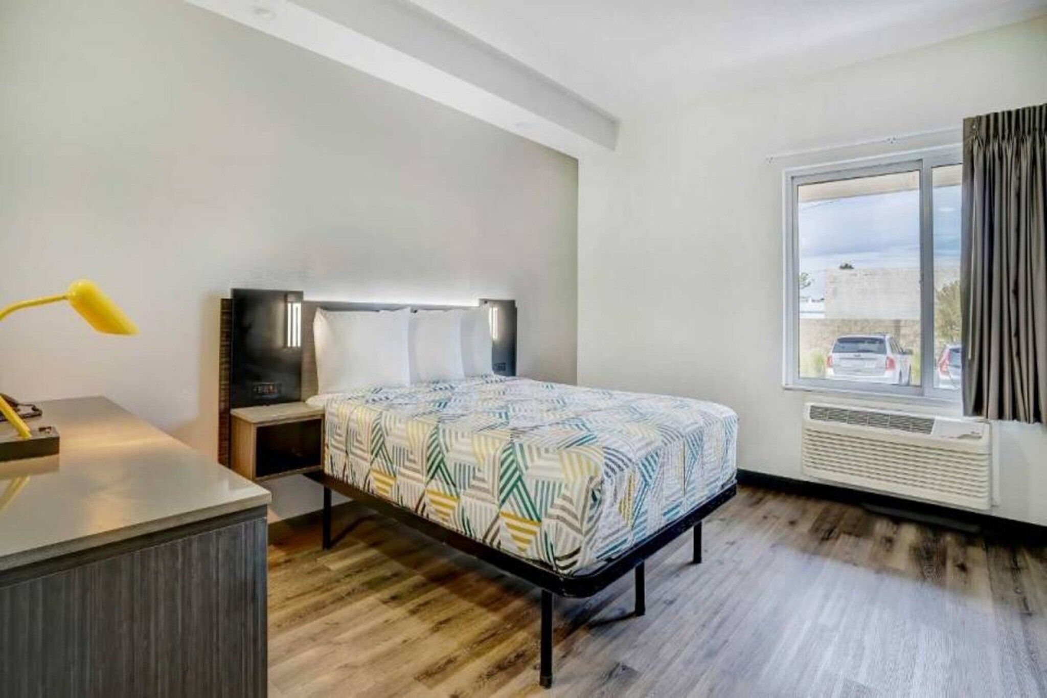 Ein Hotelzimmer mit einem Bett, einem Schreibtisch, einer Lampe, einem Fernseher, einem Fenster mit Aussicht und einem Heizkörper.