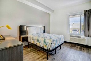 Ein Hotelzimmer mit einem Bett, einem Schreibtisch, einer Lampe, einem Fernseher, einem Fenster mit Aussicht und einem Heizkörper.