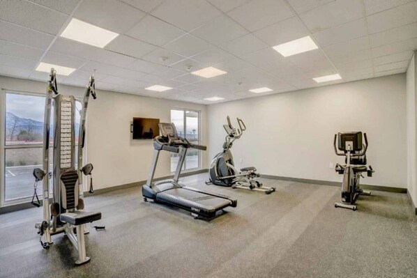 A gym with cardio machines, weight equipment, and a TV screen.