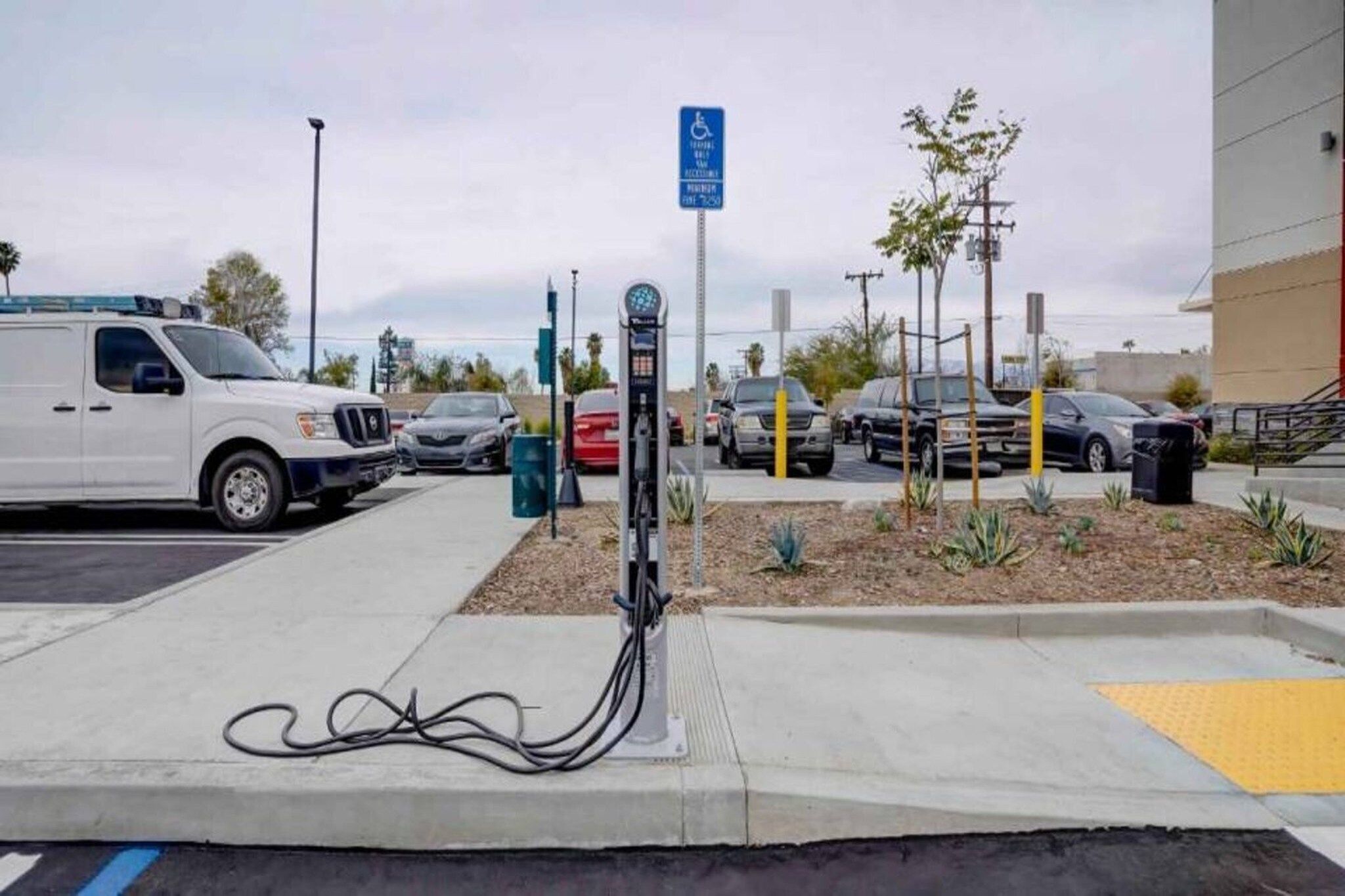 Eine Ladestation für Elektrofahrzeuge mit einem weißen Lieferwagen und mehreren parkenden Autos in der Nähe.