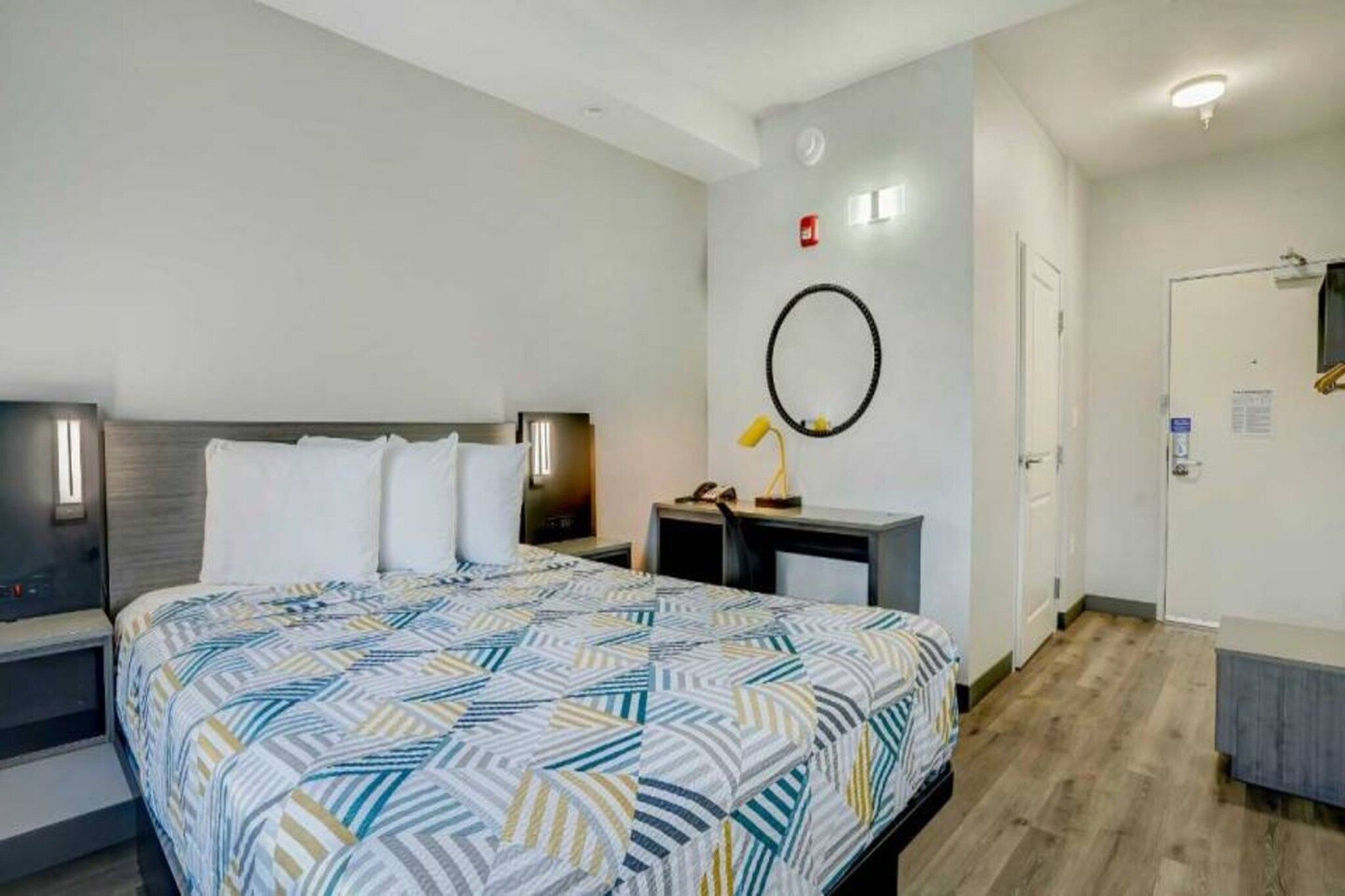 A hotel room with a bed, bedside tables, a desk, a chair, a mirror, and a door.