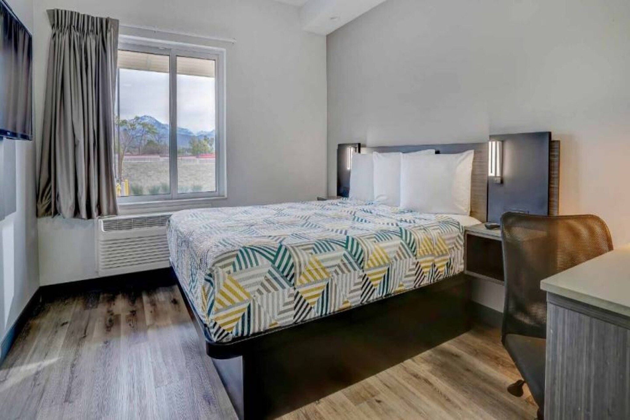 A hotel room with a bed, a desk, a chair, a TV, and a window with curtains.