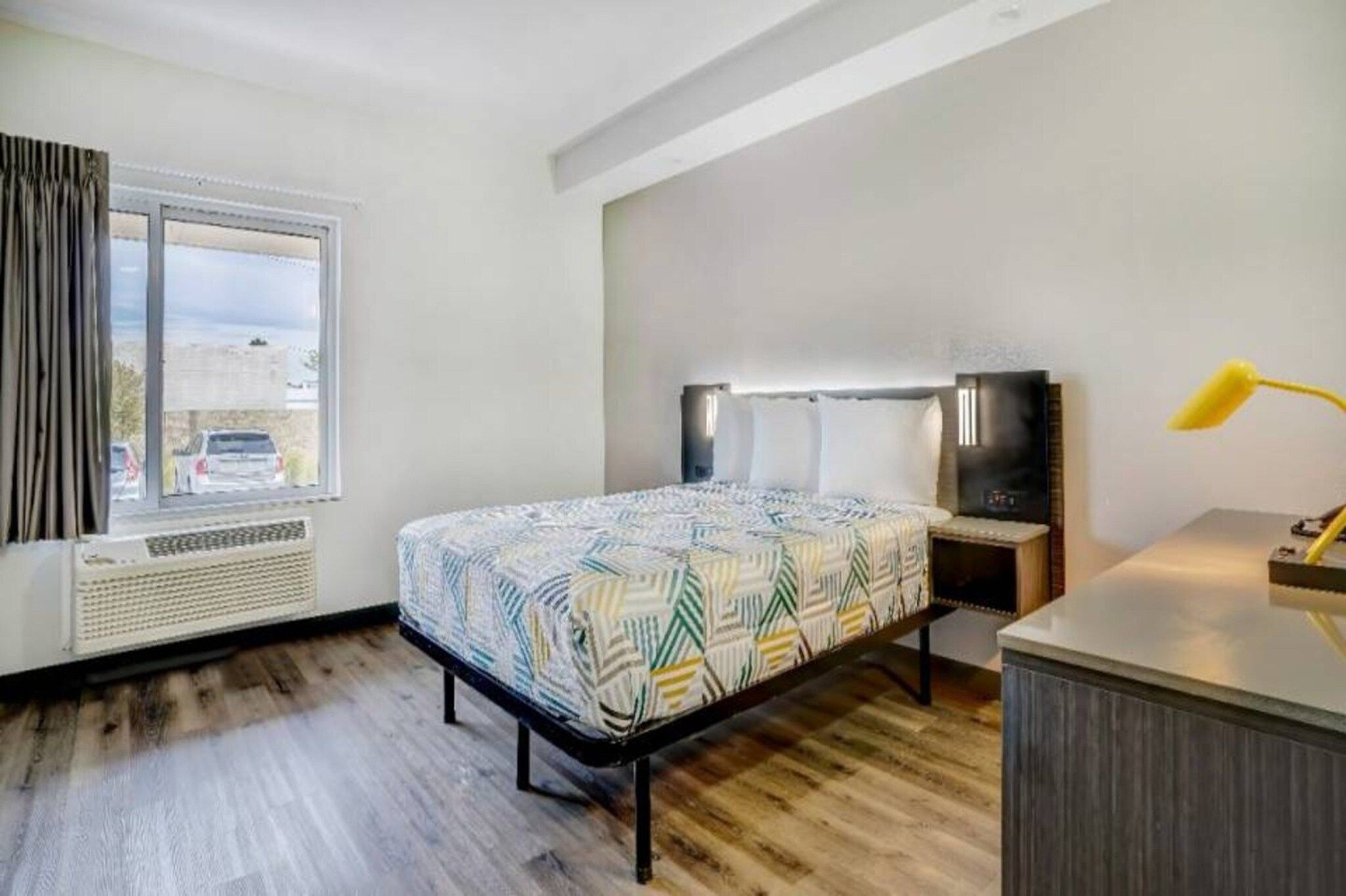 A hotel room with a bed, a desk, a lamp, and a window with curtains.