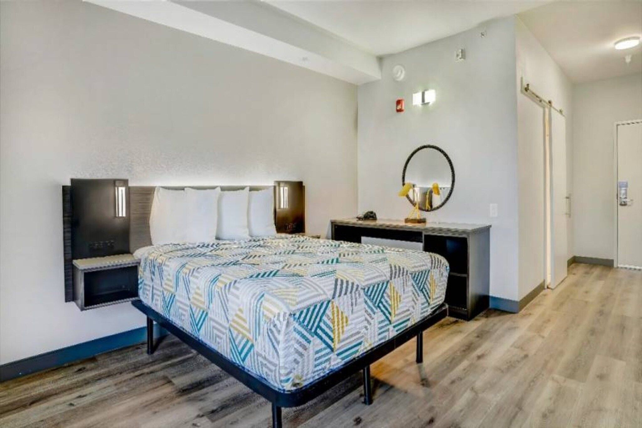 A hotel room with a bed, bedside tables, a desk, a mirror, and a wardrobe.