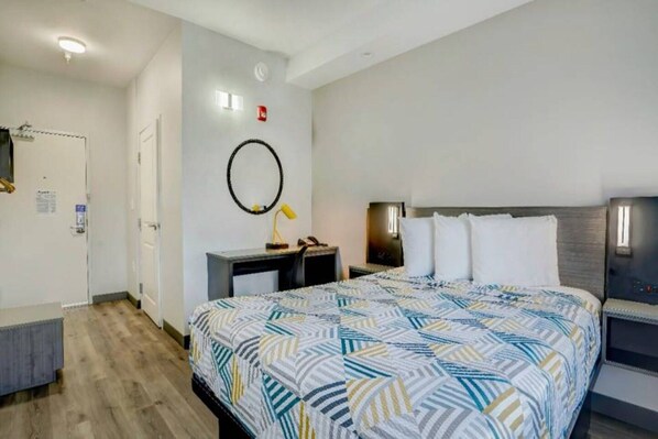 Habitación de hotel con cama, mesitas de noche, escritorio y un espejo en la pared.
