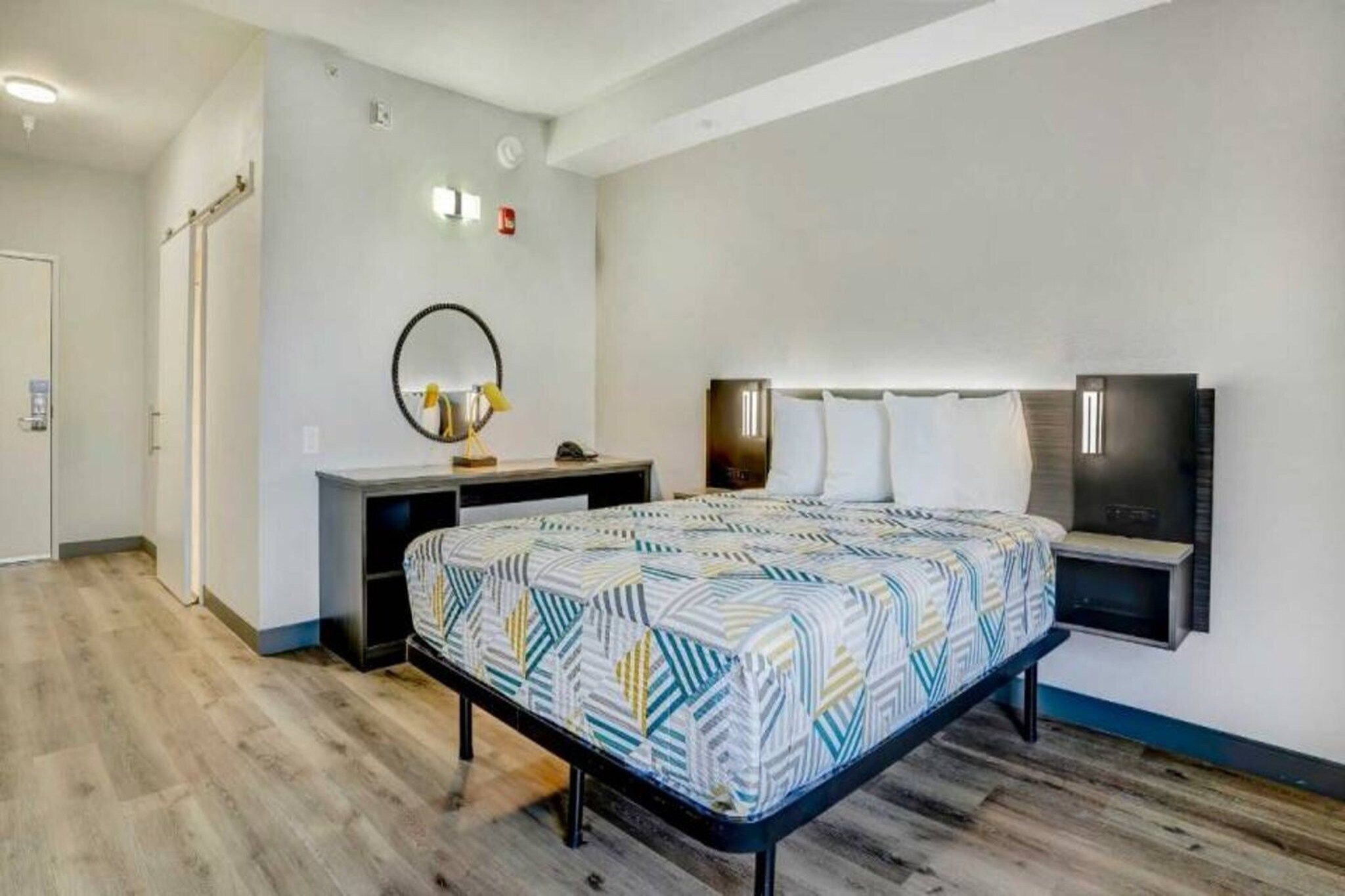 Ein modernes Schlafzimmer mit Bett, Nachttisch, Spiegel und Wandleuchte.