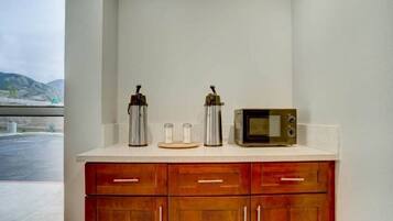 A kitchenette with a microwave, two coffee makers, and a view of a bridge and mountains.