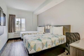 Habitación de hotel con dos camas, un escritorio, una silla, una ventana con cortinas y un televisor montado en la pared.