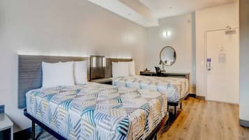 A hotel room with two beds, a bedside table, a mirror, and a door.