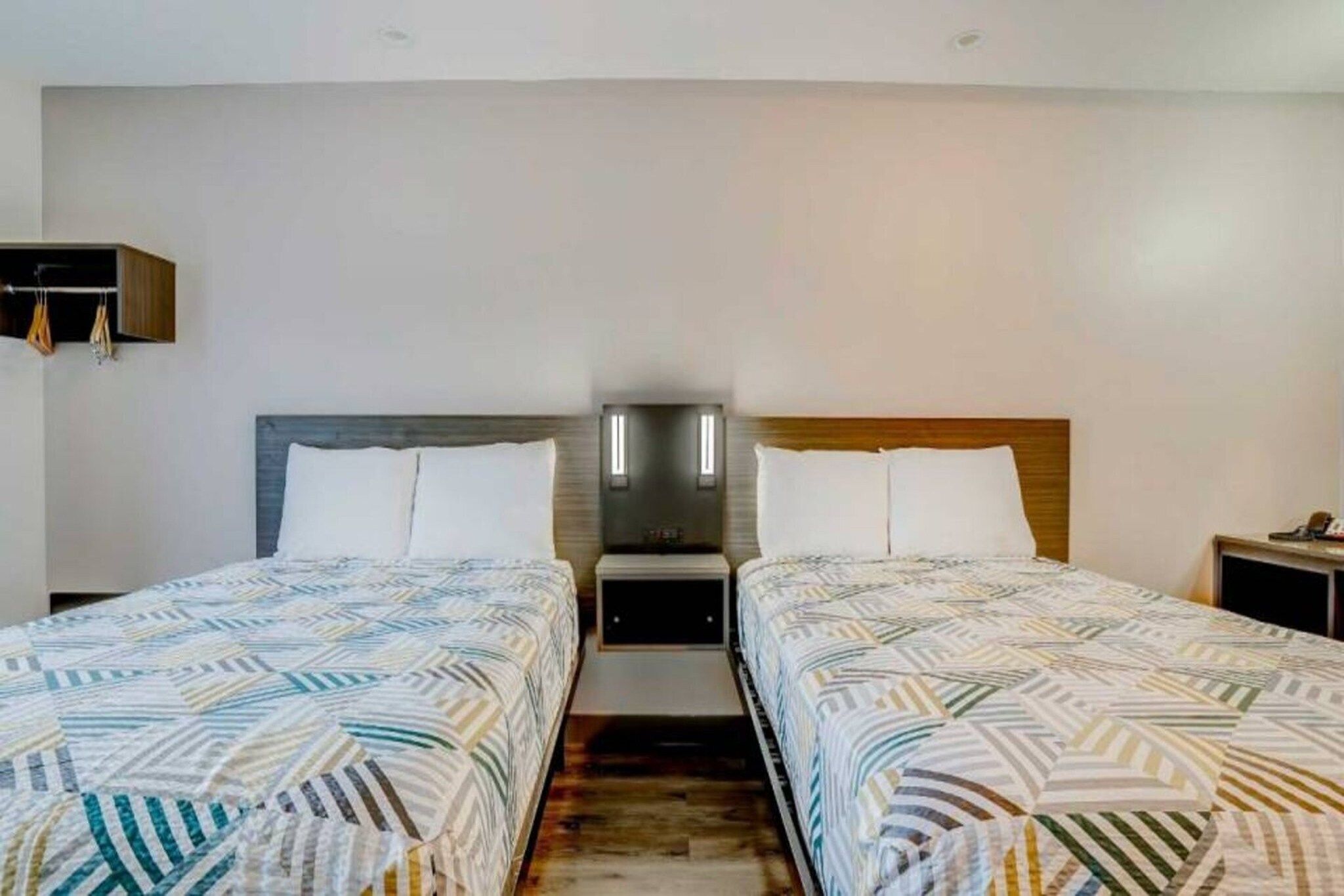 A hotel room with two beds, a nightstand, and a wall-mounted shelf.