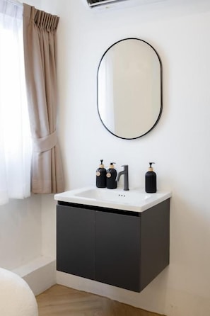 Un baño con lavamanos blanco, muebles oscuros y un espejo redondo.