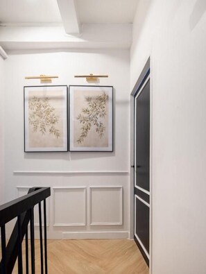 A hallway with a white wall, two framed artworks, a black railing, and a door. - Lumi Stay Pratunam (Bangkok)